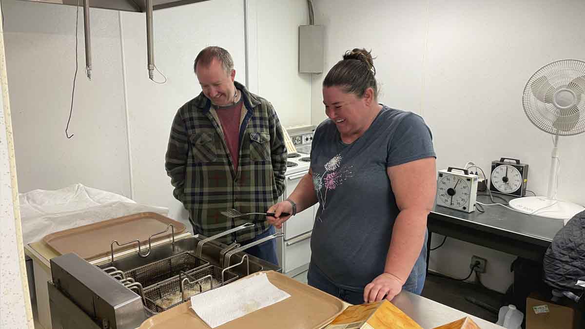 A man and women behind a potato chip fryer.